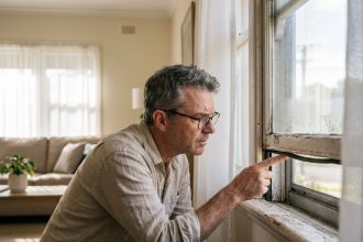 Homme inspectant le cadre d'une fenêtre ancienne à l'intérieur d'une maison pour évaluer son remplacement