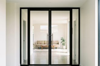 Porte battante vitrée en acier noir mat installée dans un couloir moderne aux murs blancs et sol en béton poli