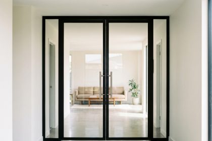 Porte battante vitrée en acier noir mat installée dans un couloir moderne aux murs blancs et sol en béton poli